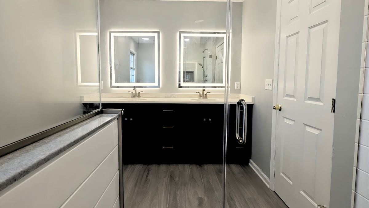 Bathroom remodel in Trappe Maryland featuring double vanity with LED mirrors, quartz countertops, frameless glass shower, and modern wood-look flooring by BCO Home Services.
