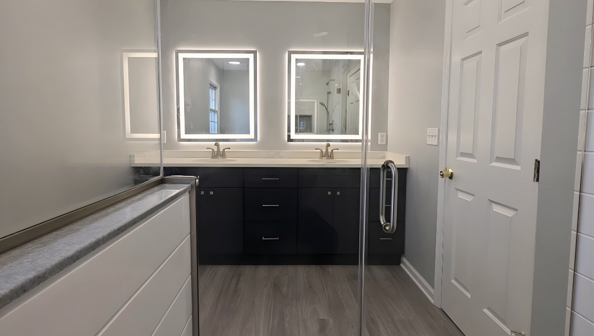Bathroom remodel in Trappe Maryland featuring double vanity with LED mirrors, quartz countertops, frameless glass shower, and modern wood-look flooring by BCO Home Services.
