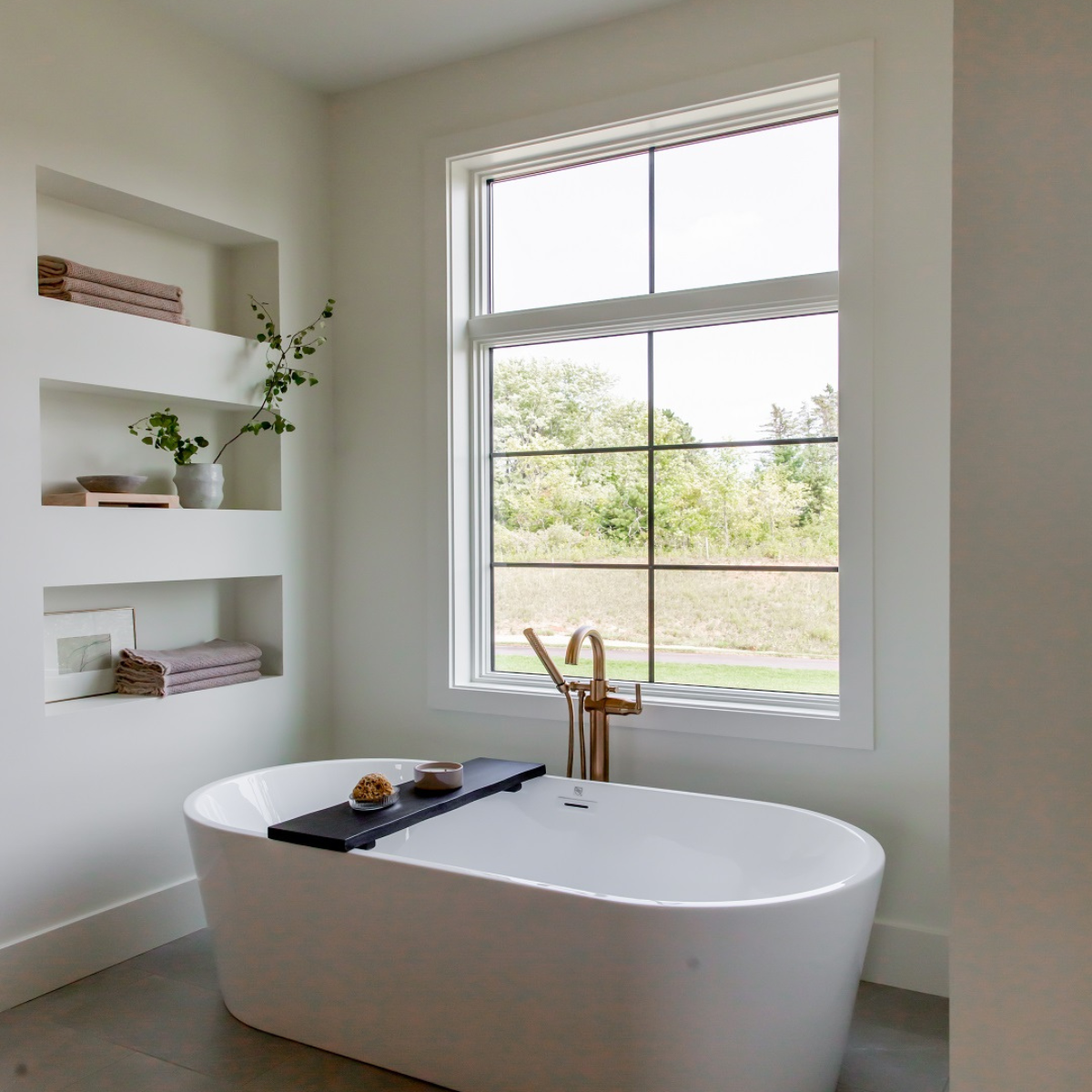 Freestanding bathtub in a modern bathroom remodel with natural light and built-in shelving