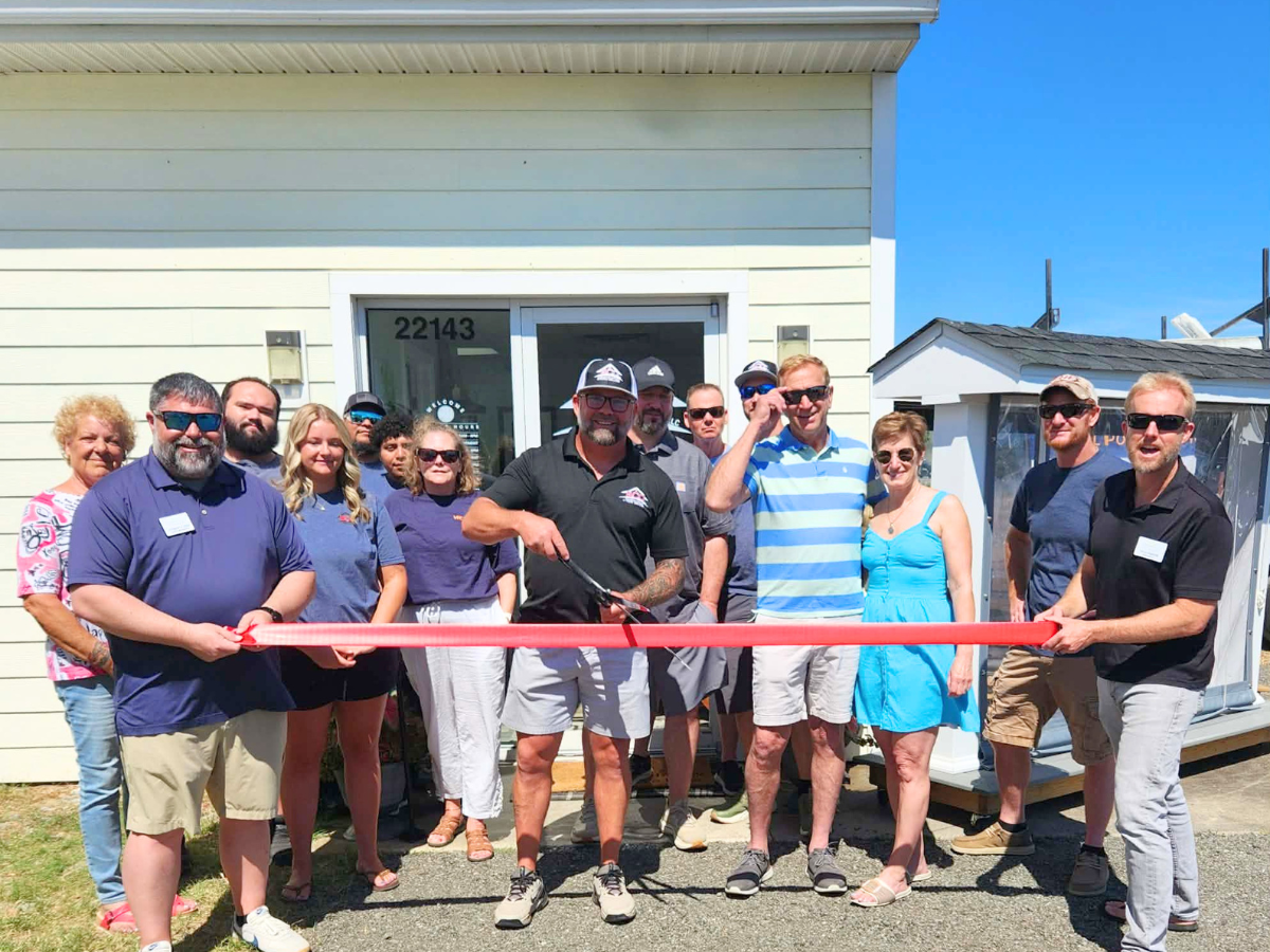 Bryan Omohundro cuts the ceremonial ribbon during the grand opening of the Home & Outdoor Living Showroom in Denton, Maryland, surrounded by team members, Chamber representatives, and community supporters.