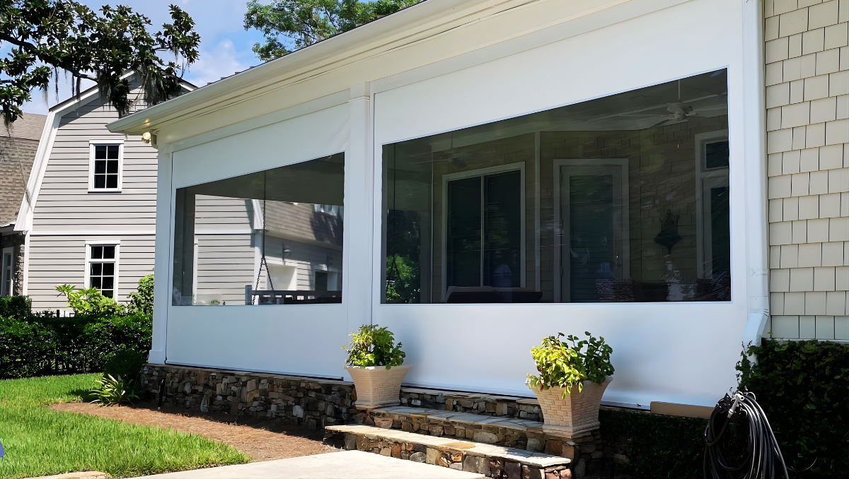 White motorized vinyl porch enclosure with clear viewing panels protecting an outdoor living space from wind, rain, bugs, and pollen.